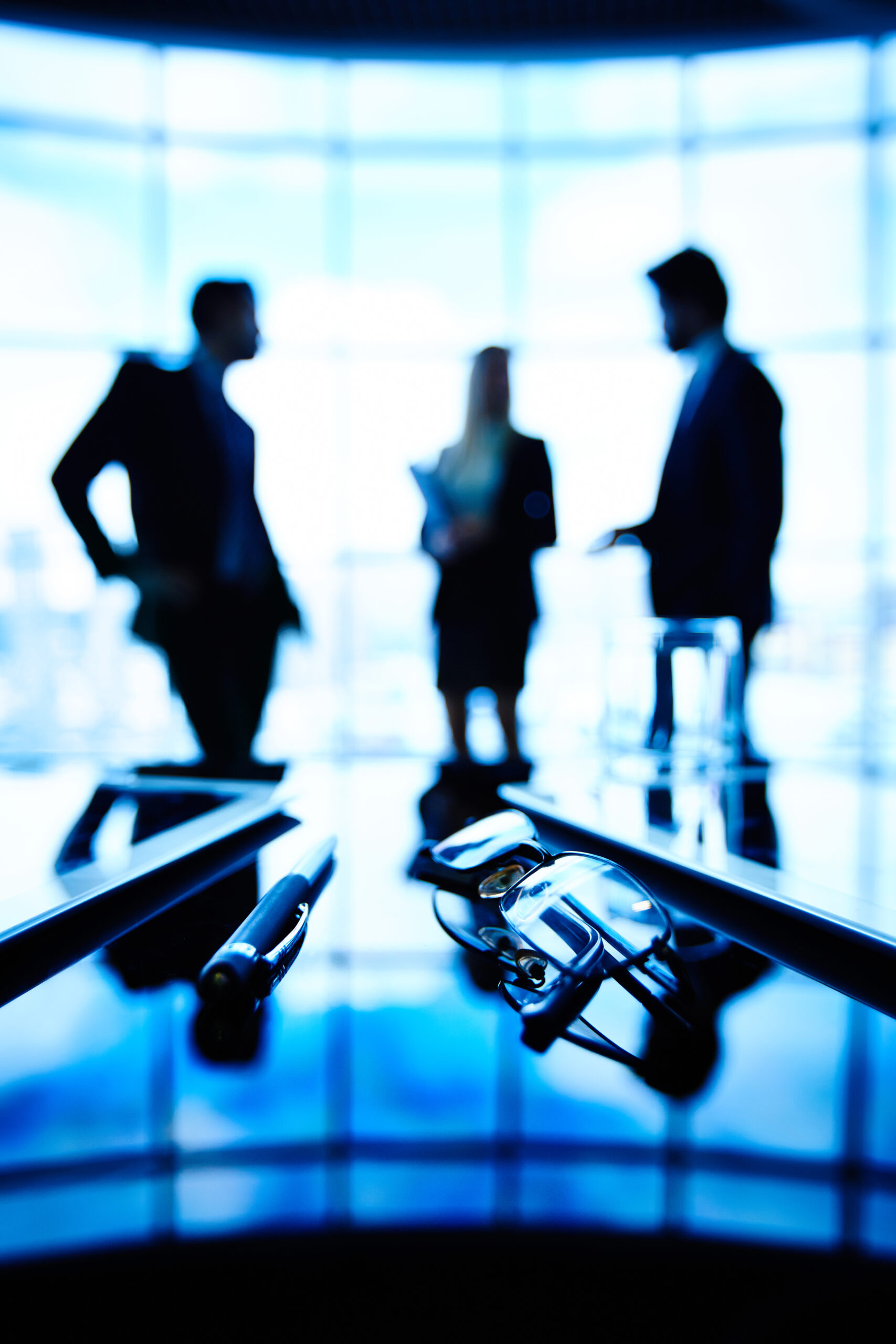 Office life Image of eyeglasses, touchpads and pen at workplace with group of businesspeople communicating on the background